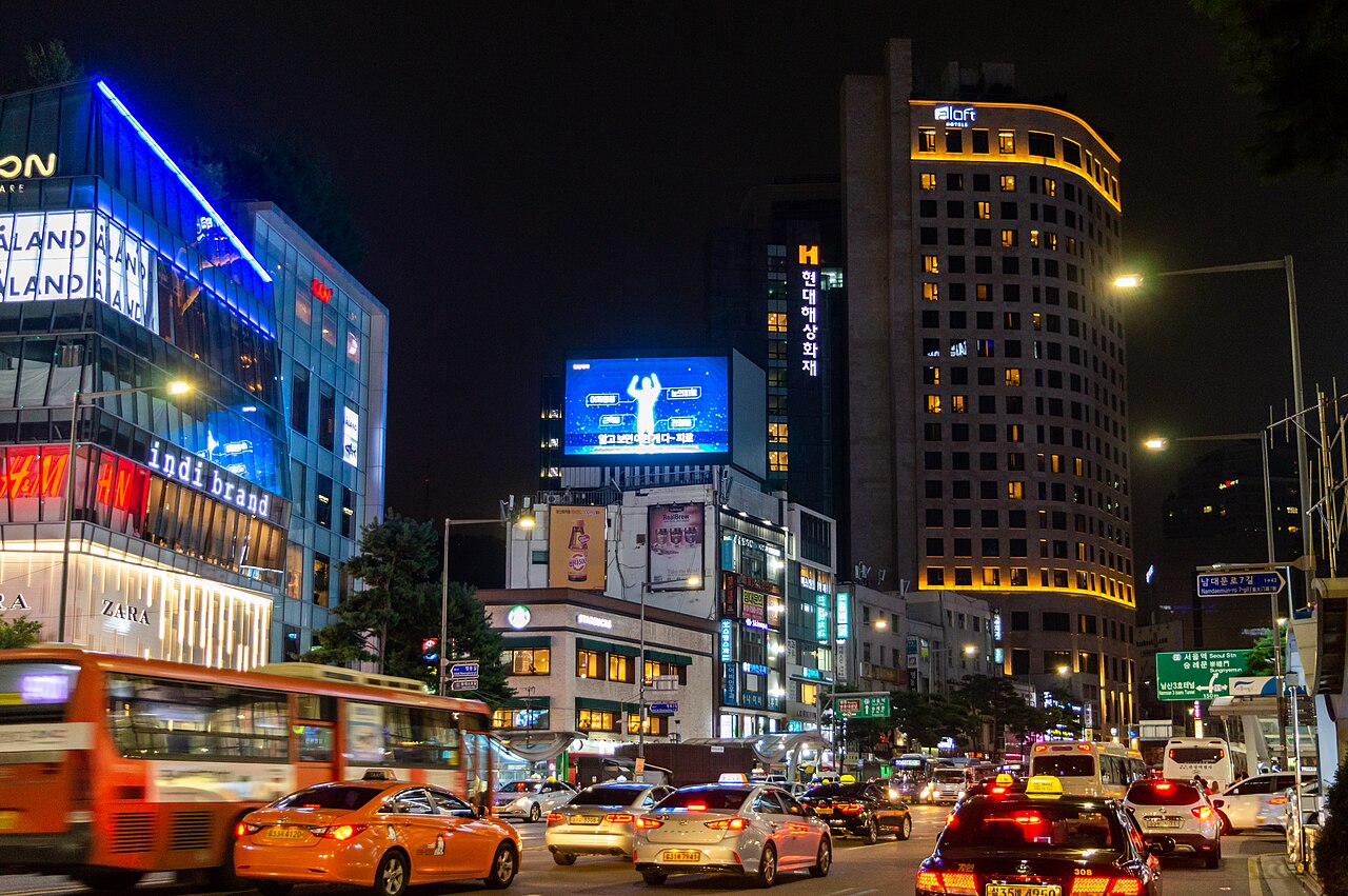 明洞夜晚街景與飯店招牌，訂房前需查同日房價的參考畫面